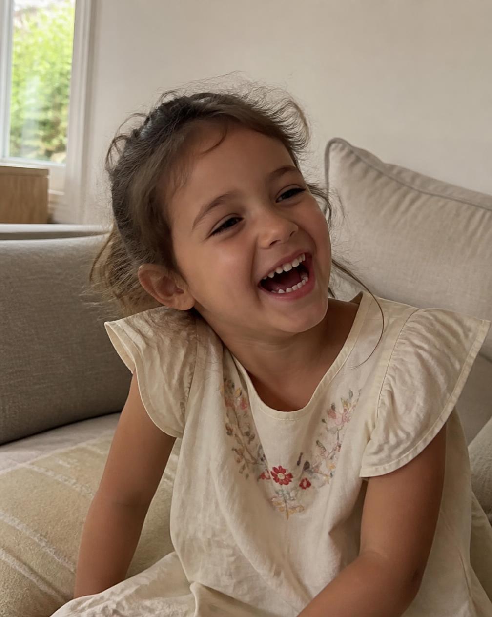 A child mid-laugh on a sofa at home.